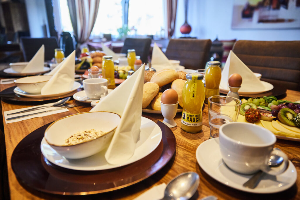 Hirschmeier-Media_20240920_00008 - WaveCult gedeckter Frühstückstisch mit Croissant Brötchen Ei Saft Obst Wurst und Käse im Strandhotel am Steinhuder Meer Eventgastronomie